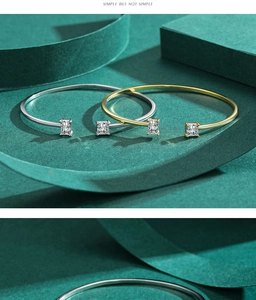 Detailed view of silver and gold open bracelets with square gemstones on green background