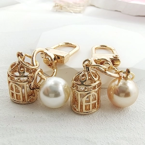 Creative gold birdcage keychain with pearl pendant on a modern hexagonal display