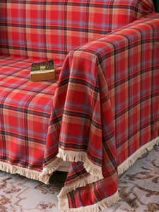 Close-up of red plaid sofa throw cover showing dense woven texture and white fringe