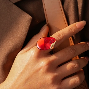 Bague artistique avec pierre en résine rouge et cadre doré sur la main du modèle