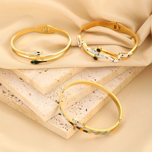 Detailed view of three gold snake-shaped bangles with white zircons on silk background