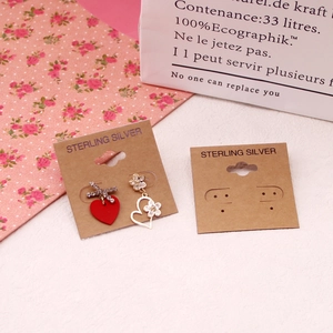 Close-up of asymmetric red heart and white flower earrings on a sterling silver card