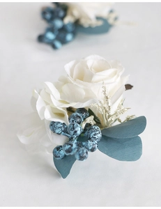 Macro shot of white silk rose wedding boutonniere with blue berries and green leaves