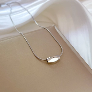 Detailed close-up of a silver rhomboid bean pendant on a sleek snake chain necklace