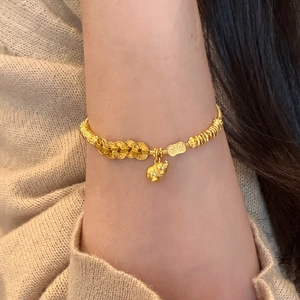 Golden hulu charm bracelet featuring coin-shaped rings and woven texture on a wrist