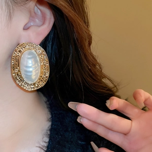 Close-up of model wearing vintage gold ridged oval earrings with white pearl inlay