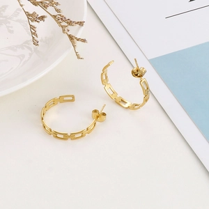 Detail view of gold-plated chain link earrings on a minimalist decorative background