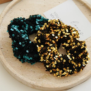 Detail of gold and deep cyan sequin scrunchies placed on a stylish beige stone tray