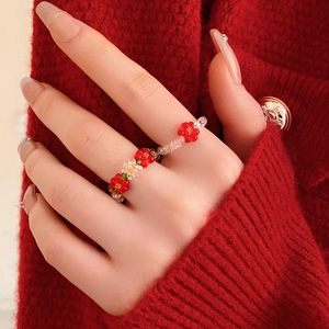 Close-up of handmade beaded flower ring with red and green beads on a red knit background