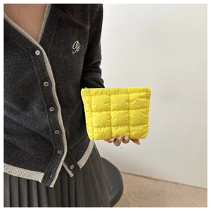 Close-up of a model holding a quilted yellow puffer clutch bag in a soft nylon finish