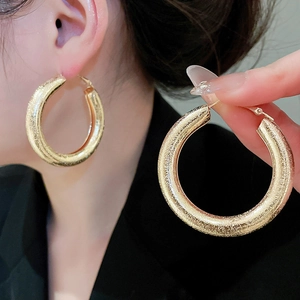 Macro detail of large golden glitter finish hoop earrings with polished metal texture