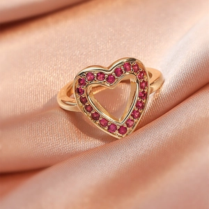 Macro view of gold heart ring featuring pave-set red gemstones on peach satin