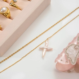 Détail du collier croix en or 18 carats avec perle baroque sur une boîte à bijoux en velours