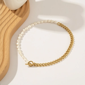 Detail of OT buckle closure on half pearl and gold chain bracelet over wooden decor