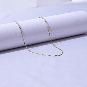 Detail of 18k gold lip chain necklace with green enamel oval beads on white display