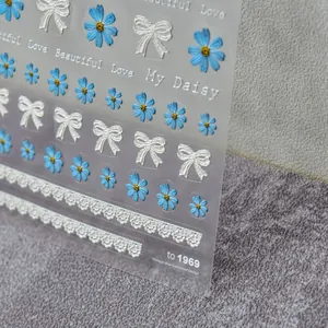 Macro shot of 5D embossed nail stickers with light blue daisies and lace bows