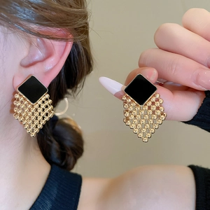Detail view of woven diamond stud earrings with black enamel and gold bead tassels
