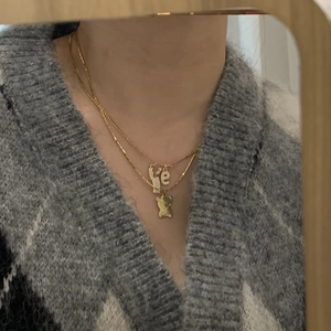 Detail of layered gold necklace with letter L, e, and bear charms on a knit sweater