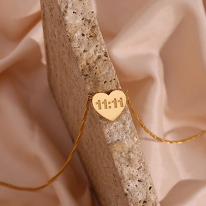Detailed view of 11:11 gold plated heart necklace draped on stone with silk background