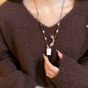 Detail of a brown woven necklace with a white bear pendant and colorful tassel on a sweater