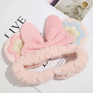 Close-up of soft pink plush headband featuring embroidered flower bow and coral fleece texture