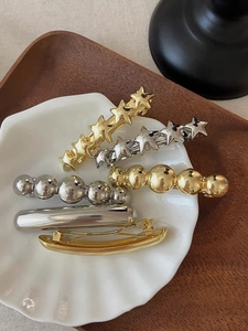 Close-up of golden and silver metal star hair clips displayed in a white shell tray