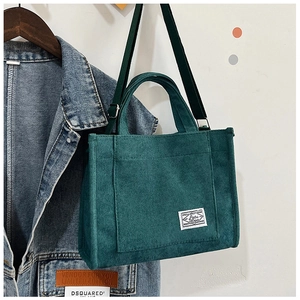 Detail of dark green corduroy handbag showing texture, front pocket and fabric label