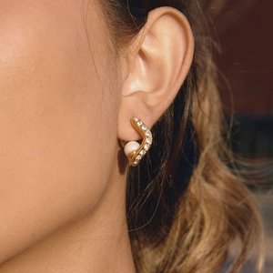 Elegant gold wavy earrings with zircon accents and pearl pendant worn by model