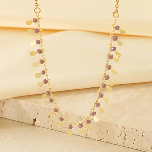 Detail of gold fringe necklace with water drop leaves and purple beads on stone