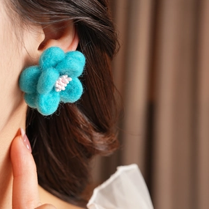 Gros plan d'une boucle d'oreille fleur en laine bleue sur un mannequin femme