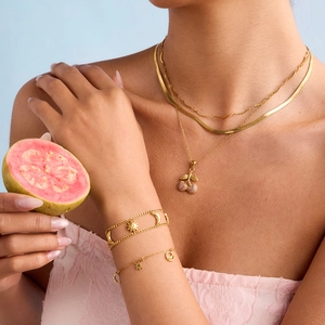 Close-up of layered 18K gold-plated necklaces with a sparkling cherry pendant on a model