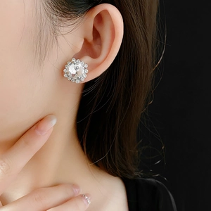 Close-up of sparkling silver round stud earring with large centered zircon on model's ear