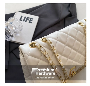 Close-up of white quilted leather texture with gold metal chain and rotary clasp detail