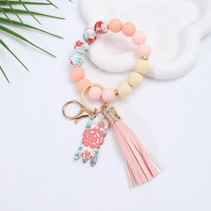 Pink silicone beaded keychain bracelet with PU tassel and gold hardware on white background