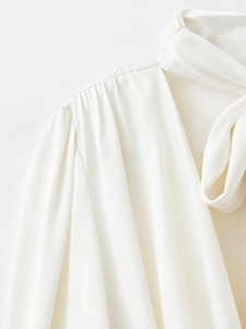 Détail d'une blouse en satin blanc avec plis aux épaules et ruban de col élégant