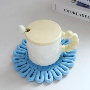Detailed close-up of a blue knitted flower coaster under a white ceramic mug set
