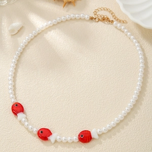 Detail of beaded necklace featuring white pearls and red fish charms on textured background