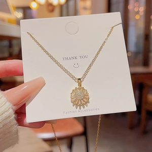 Golden sunflower necklace with sparkling zircons held against a warm light background