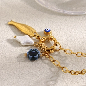 Close-up of gold fish charm with blue evil eye and pearl beads on O-chain necklace