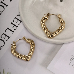 Close-up of golden heart-shaped hoop earrings with elegant twisted rope texture on a plate