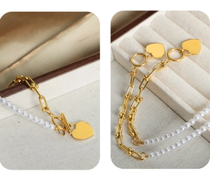 Detail of the heart pendant on gold U-link chain and white pearl bracelet with OT buckle