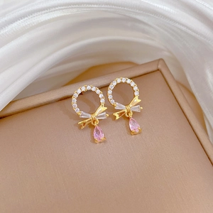 Detail of gold bow earrings with white crystals and a pink teardrop zircon pendant