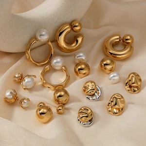 Golden stainless steel earrings and rings with white pearls on elegant beige silk fabric