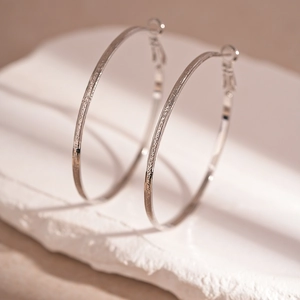 Macro shot of large silver geometric earrings with hammer texture on a white stone base