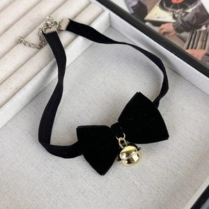 Gros plan du choker en velours noir avec un nœud et un pendentif clochette dorée