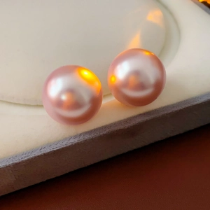 Macro shot of pink round pearl earrings with metallic luster on jewelry display box