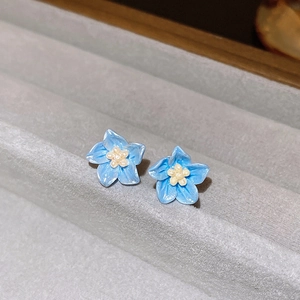 Gros plan de boucles d'oreilles myosotis bleu clair avec pétales en émail et perles