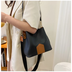 Détail d'un sac seau en cuir noir avec bordure marron et bandoulière rayée