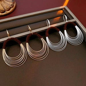 Detail of multilayer oval hoop earrings in gold and silver on a brown leather tray
