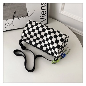 Close-up of black and white checkerboard canvas cylinder bag with a woven shoulder strap